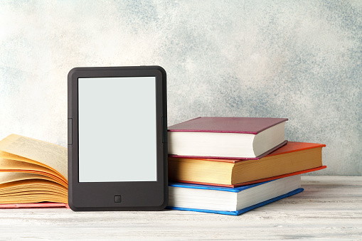 Digital tablet with a stack of books on gray background close up