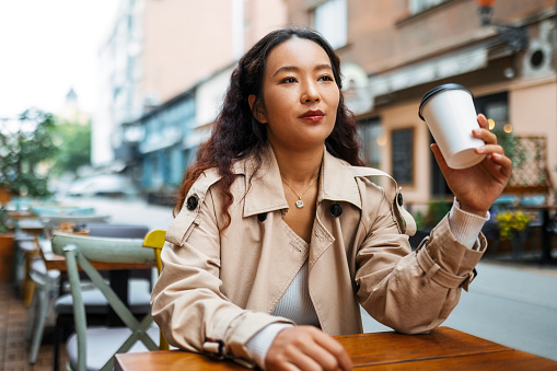 Young Asian woman drinking coffee in sidewalk cafe