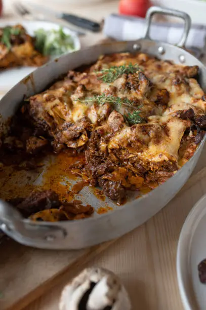 Delicious lasagna with braised and shredded meat, gravy, mushrooms and cheese topping. Served ready to eat in a rustic roasting pan or casserole dish on wooden, table background. closeup