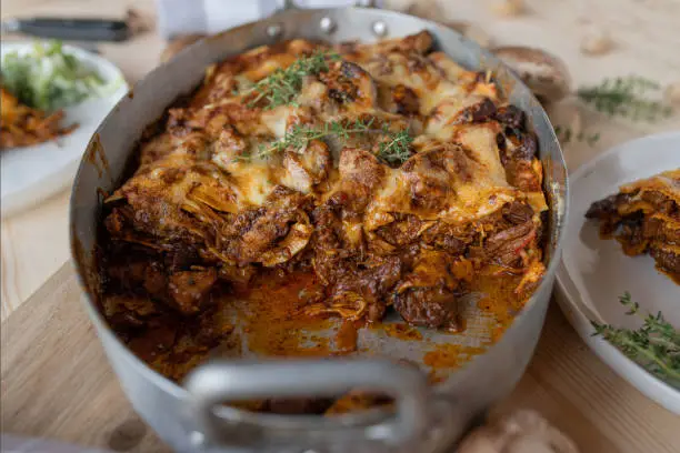 Delicious pasta casserole with lasagna noodles and braised turkey meat, mushrooms and cheese topping. Served ready to eat with cross section view on a dinner table.