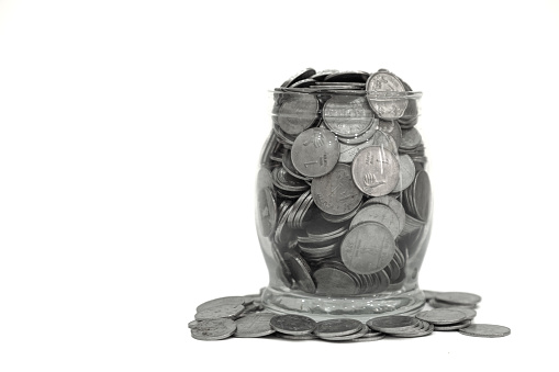 Indian Coins spilling out of a glass jar on white background