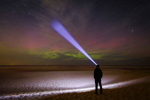 A man observing the Northern Lights on the beach of the Baltic Sea in Sztutowo. Poland