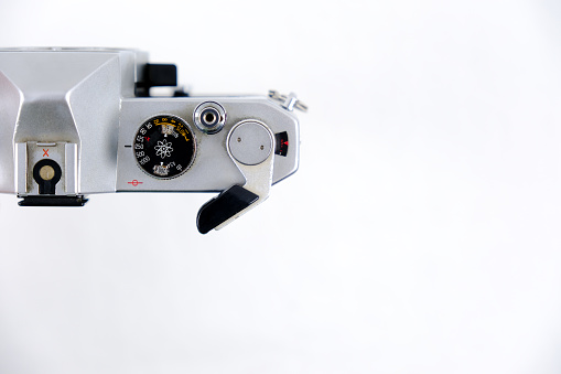 A film of 36 is mounted on the 1976 model analogue camera. Top shot. The background is one color. Gray silver, black color camera.In the background is a box of 36 films. The focus is on the camera, a hand is holding the camera.hand holding camera