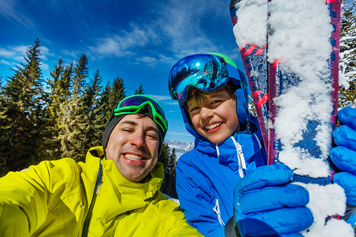 Father and happy little child boy take selfie photo smiling holding alpine ski wearing mountain sport outfit