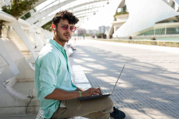 istock A view of a man with a lap-top working outdoors seated, dressed casually in a light blue shirt, sunglasses and city background. 1720117121