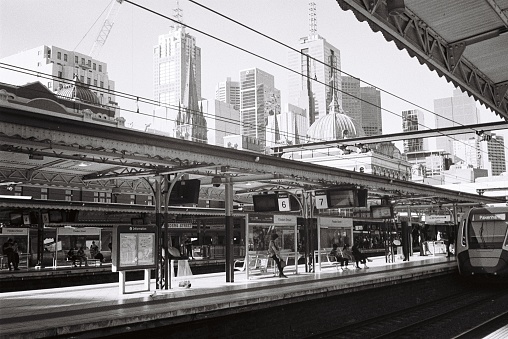 Black and white film photo from inside Flinders st Station. Photo taken on the platform with the Melbourne skyline in the background.