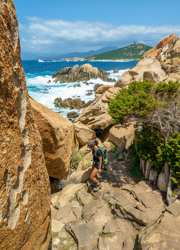 Corse, France - 1 July 2023 - Corsica is a big touristic french island in Mediterranean Sea, with beautiful beachs and mountains. Here a view of the Sentier du littoral from Campomoro with girl hiker and waves on the rocks