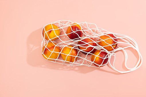 Nectarines in a white string bag on a colorful background