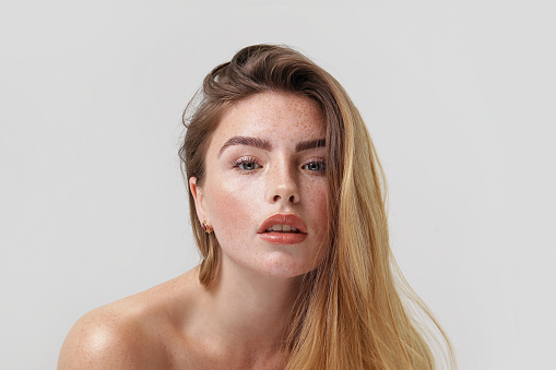 Studio beauty portrait of young natural woman with freckles on her face. Girl looking at the camera. A lot of copy space. Skin care concept. Ideal, delicate makeup with lipstick.