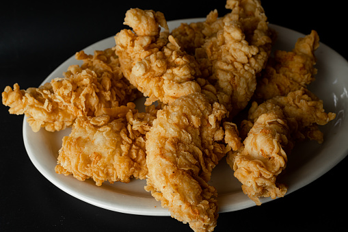 Crispy fried chicken in a plate isolated on black background. Fresh crunchy fried chicken on a white plate. Delicious hot and crispy fried chicken. Image about food of fast food restaurant.