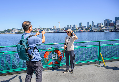 Tourists taking photos using smartphone on the ferry at Elliott Bay. Seattle skyline and the historic Space Needle in the background. Seattle. Washington State.