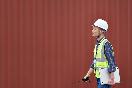 One asian male warehouse worker walking at cargo container  red backgrounds in commercial dock.