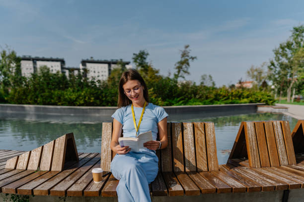 istock Young female nurse reading a book on a park bench 1720205271