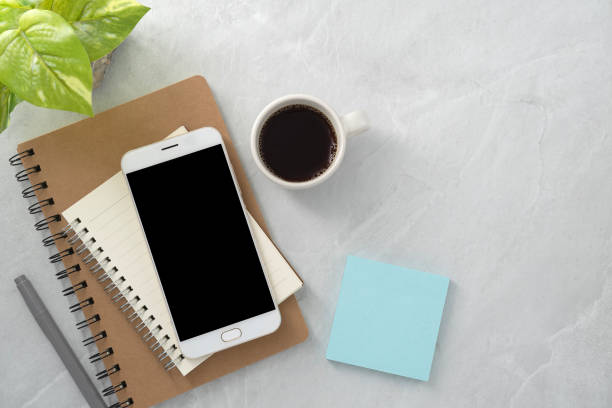 istock Mobile phone with blank mockup screen and book and coffee on stone texture background.Work desk. Top view. Flat lay. 1720215184