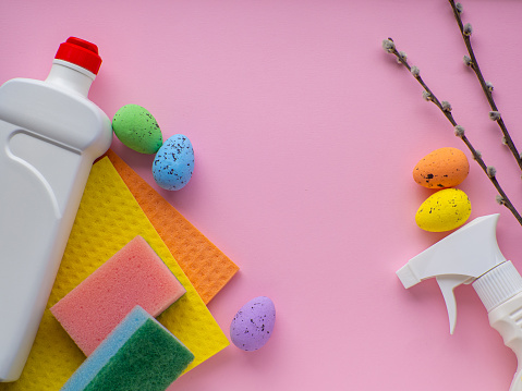 Happy Easter and cleaning concept. Detergent with Easter decoration on pink background with copy space. Easter greating card. Flat lay. Cleaning stuff, colorful eggs and willow twigs. Housekeeping