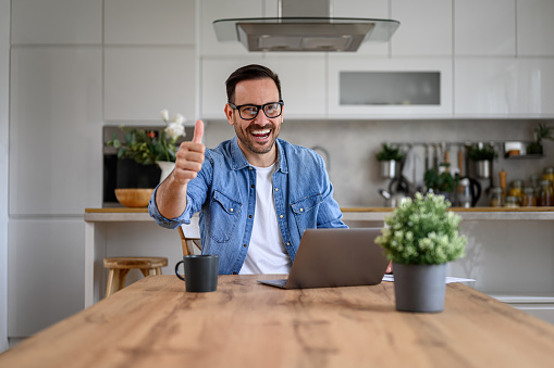 Handsome businessman showing thumbs up sign while working over laptop on desk in home office
