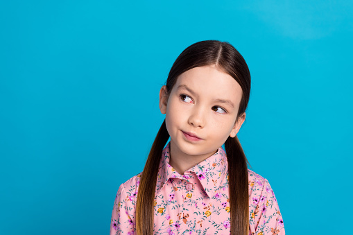Photo portrait of lovely schoolkid girl look interested empty space wear trendy pink flower print garment isolated on blue color background.