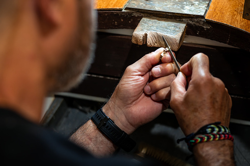 Goldsmith working and creating in his crafting gold jewelry workshop. Jeweler liming a silver jewel.