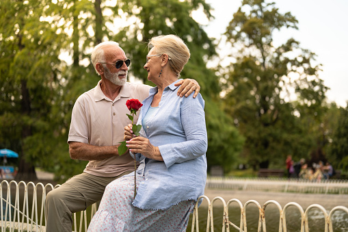 Senior couple in park, man giving red rose to woman