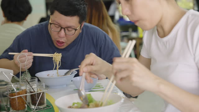 Asian lady and Asian man eating noodle in local restaurant