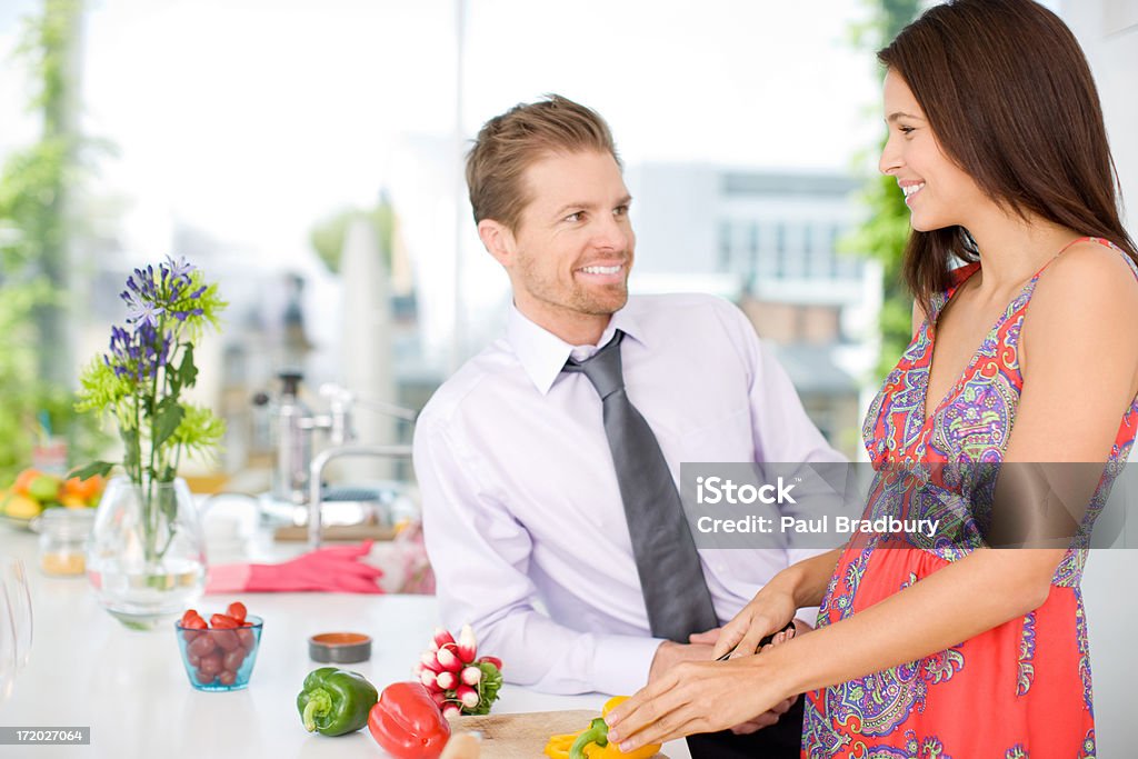 Marido hablando de mujer mientras la paciente parte de las verduras en la cocina - Foto de stock de 25-29 años libre de derechos