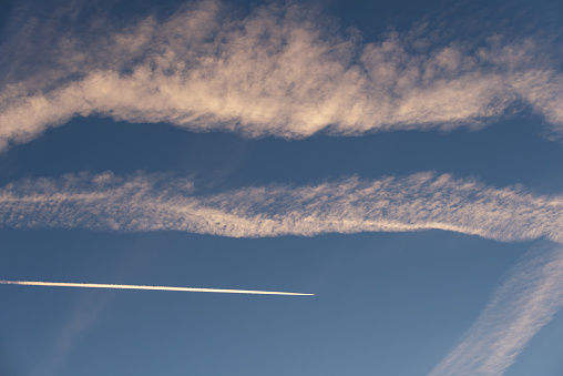 Landscape of a beautiful blue sky with clouds, white vapor trails and a plane in the evening. Nature.