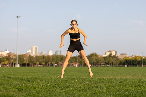 Pretty young athlete lady is jumping exercise on the grass.