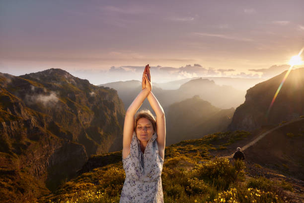 Young smiling woman meditating with her arms raised during spring day on a mountain at sunset. Copy space.