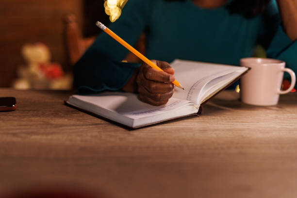 Close up shot of unrecognizable young woman sitting at home office desk, contemplating her New Year's resolutions and writing them in a diary.
