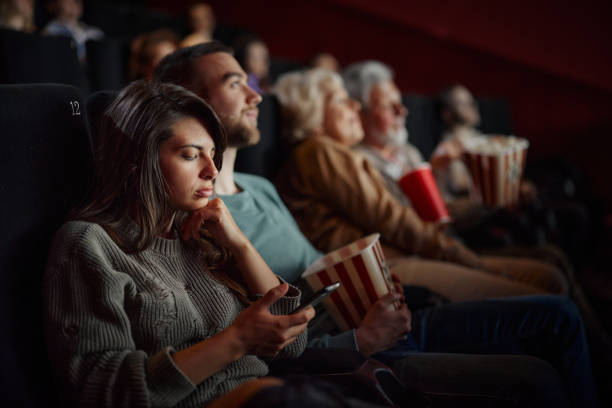 istock Bored woman using mobile phone during movie projection in cinema. 1720334829