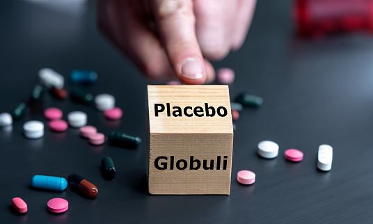 Symbol that homeopathic medicine has an placebo effect only. Hand turns cube and changes the German word 'Globulin' (globule) to 'placebo'.