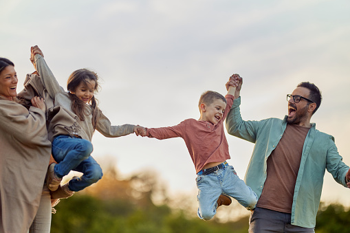 Happy parents having fun while holding hands with their kids while they are jumping during spring day in nature. Copy space.