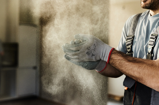 Close up of unrecognizable construction worker clapping his hands while cleaning dust from his gloves during home renovation process. Copy space.