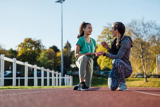 Front view of a young female child crouched down and ready to begin her sprint on an athletics track outside Wentworth Leisure Centre in Hexham, North East England. She is wearing sports clothing and she's focused on her sprint. Her mid adult female coach is motivating her before she runs.

Video also available of this scenario.