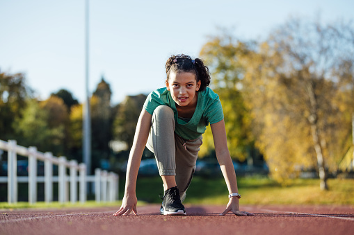 Front view of a young female child crouched down and ready to begin her sprint on an athletics track outside Wentworth Leisure Centre in Hexham, North East England. She is wearing sports clothing and she's focused on her sprint.

Video also available of this scenario.