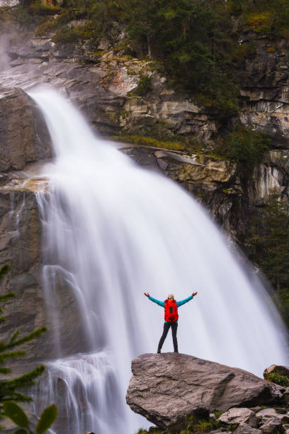 istock woman with backpack and outstretched arms standing on rock at waterfall 1720425775