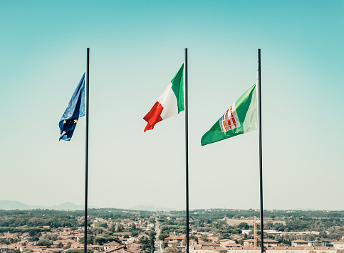 Flags flying in the wind at Cortona, Tuscany, Italy. From the left, European Union flag, Italian flag, Umbria region flag.