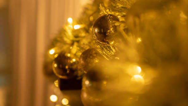 baubles fairy lights on christmas tree in evening room closeup. festive ornament with shiny balls and glowing garland on fir tree branch. holiday decoration with sparkling toys and lights on xmas eve - christmas tree branch imagens e fotografias de stock
