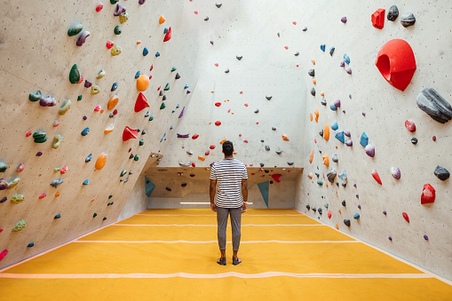 A wide angle rear view of a man looking at the expansive climbing wall at an indoor climbing centre in Newcastle Upon Tyne in the North East of England. The wall looks overwhelming but he has the confidence to go for it!