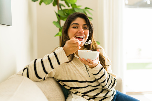 Attractive happy hispanic woman smiling and enjoying eating healthy food at her cozy home for her wellbeing