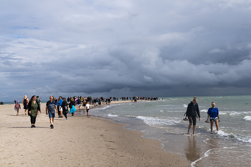 Many people walk along the seashore or ocean on a stormy cloudy day. Skagen, Denmark - September 25, 2023