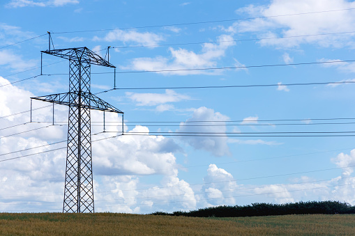 Electricity concept. High voltage power line pylons, electrical tower on a green field with blue sky.