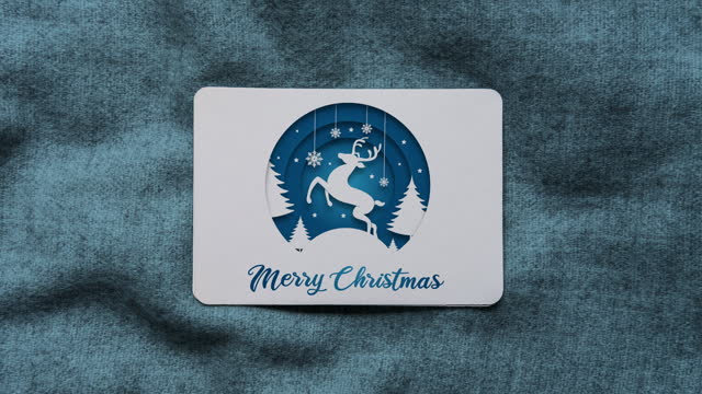Blue coloured paper cut style reindeer and Merry Christmas text animation on Christmas card