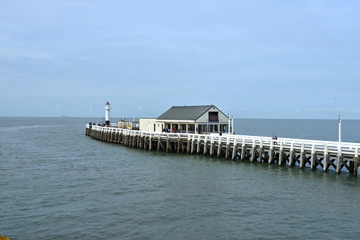 Blankenberge, West-Flanders, Belgium-September 30, 2023: tourists walking on the pier. White beach house restaurant at the ende of the Oosterstaketsel Pier in front of the sea