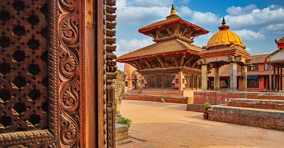 The most famous Durbar square, Bhaktapur's,  scattered with temples and palaces. On the foreground detail of a wood curved door. All three Durbar squares in Kathmandu valley are UNESCO world heritage sites.