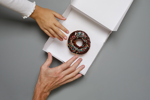 Two hand holds a glazed donut on a gray background. Chocolate donut. Top view.