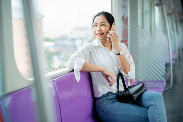 istock Young Asian woman using smartphone talking someone with smile while sitting on seat in metropolitan sky train and looking city scape view outside window, woman connecting and using technology in smart city concept. 1720663161