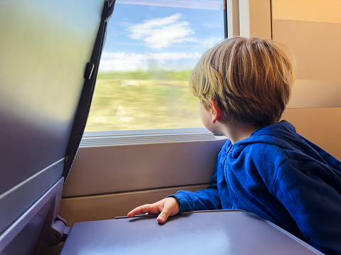 Little boy sit and looking at the window inside high speed train staring at rural landscape