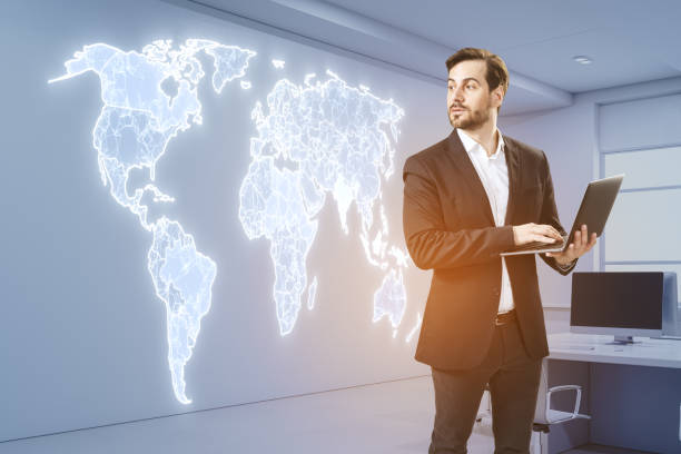 istock Attractive young european businessman using laptop in office interior with creative glowing polygonal map hologram. Global community and network concept. 1720668391
