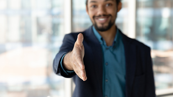 Close up focus on African American hr manager in suit hand extending for handshake, smiling businessman entrepreneur greeting or offering cooperation, welcoming new employee at job interview